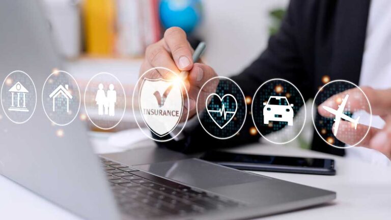 A couple reviews homeowners insurance documents at their kitchen table with a laptop and paperwork spread out.