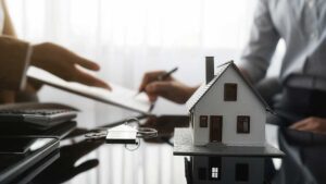 An insurance adjuster reviews accident photos and claim documents with a homeowner at a kitchen table.