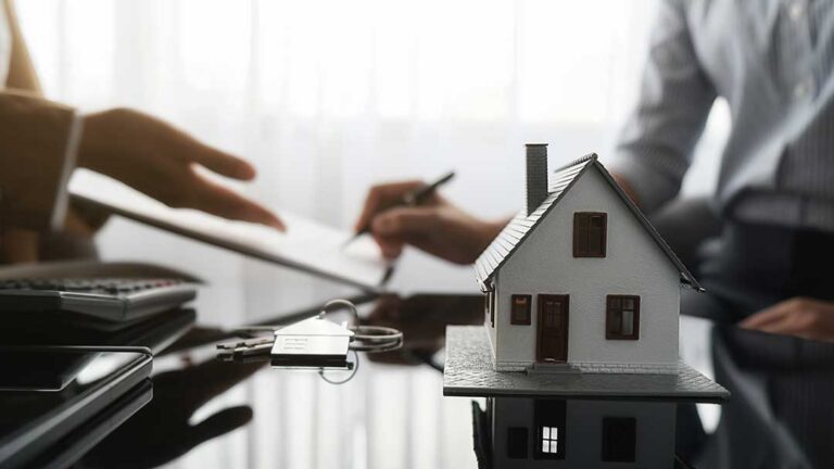 An insurance adjuster reviews accident photos and claim documents with a homeowner at a kitchen table.