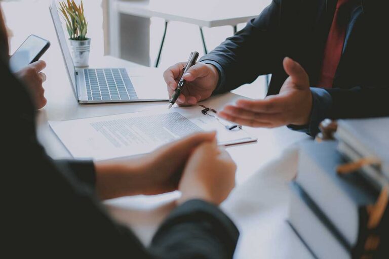 Family members review a life insurance policy, death certificate, and funeral expense papers at a kitchen table.